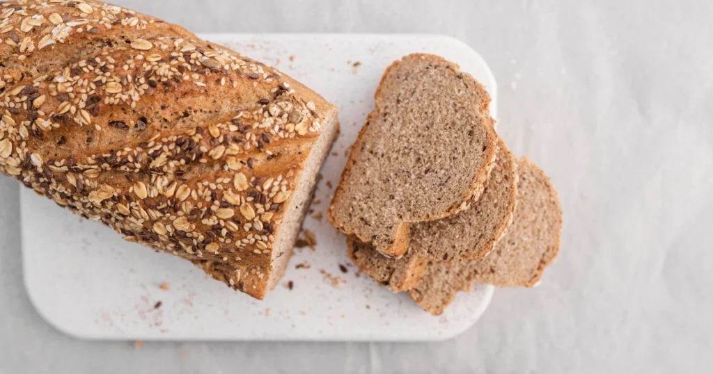 Close-up of sliced soft sourdough sandwich bread with a golden crust and seed topping, placed on a white cutting board.