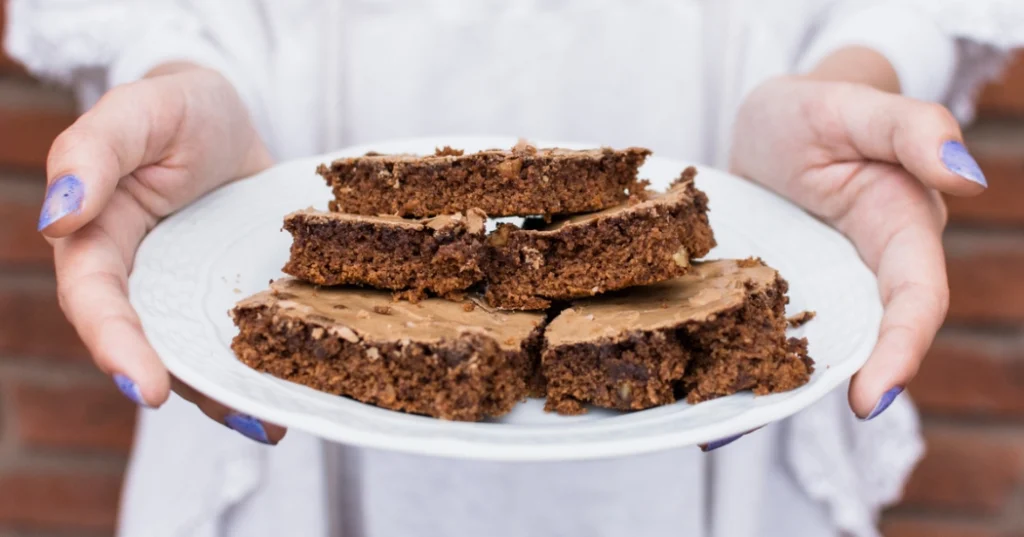 A plate of freshly baked brookies held by a person with purple-painted nails, featuring a crispy top and a moist chocolatey texture.