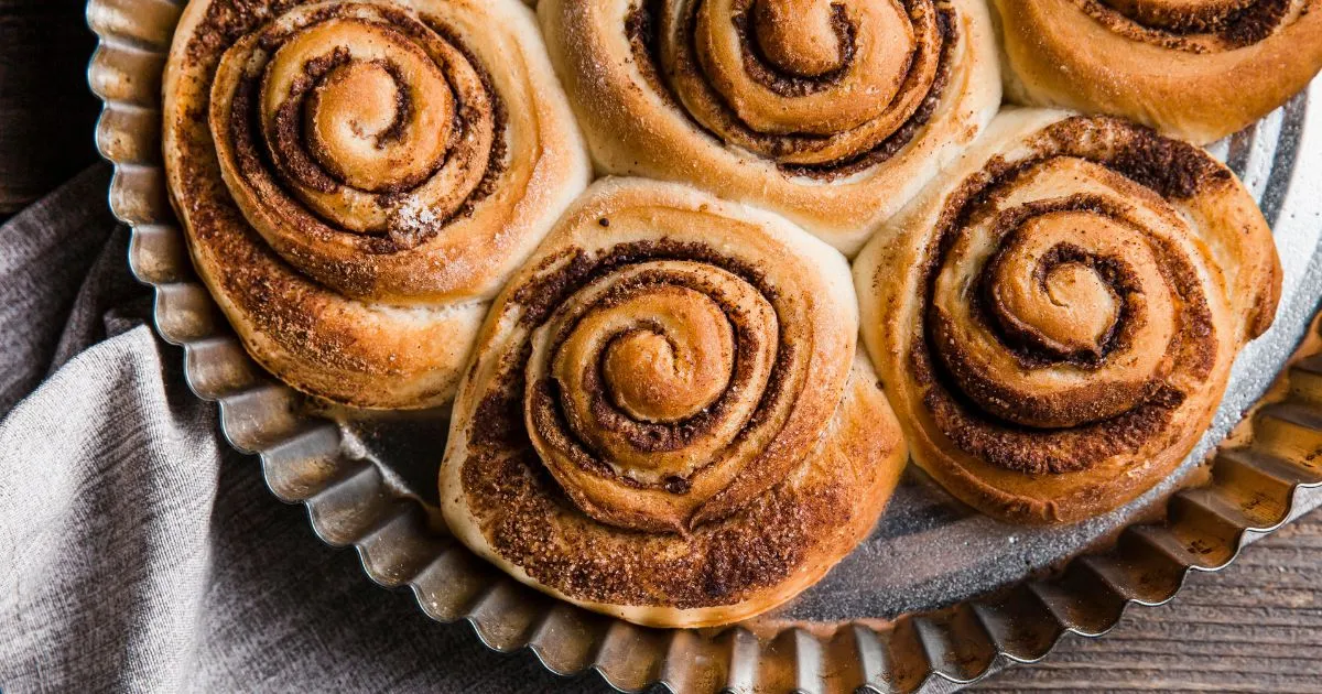 Freshly baked sourdough cinnamon rolls with golden-brown swirls of cinnamon and sugar, served in a round metal baking dish.