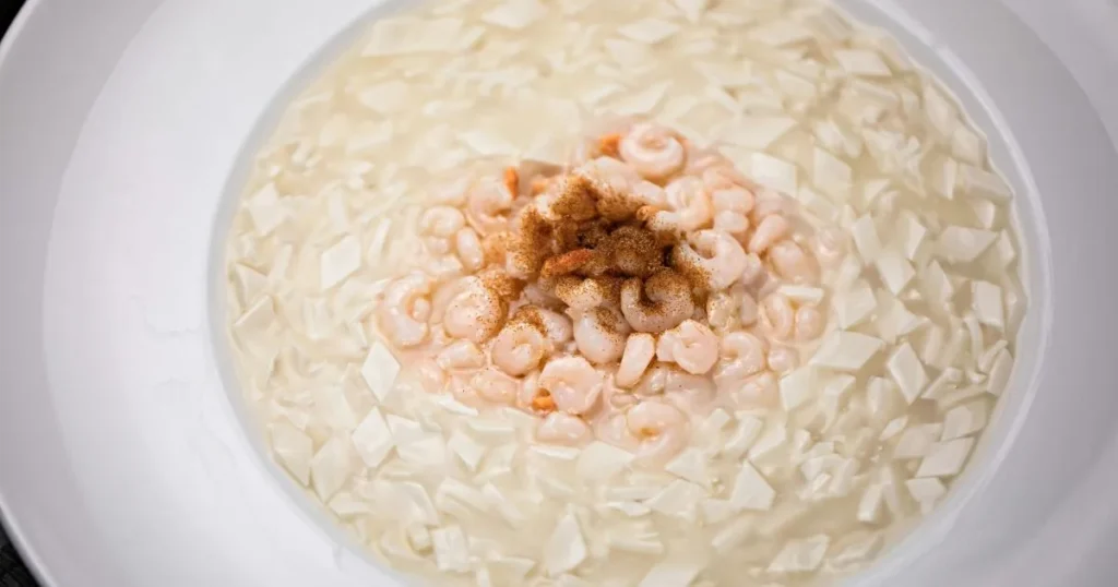 A bowl of raw shrimp soaking in milk, surrounded by diced tofu, ready for preparation.